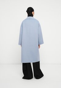 Abrigo azul claro de corte oversized con un gran cuello, fabricado en tejido texturizado. Mangas largas y un corte recto, combinado con pantalones anchos negros.