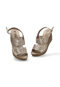 Sandalias de cuña beige con acentos metálicos decorativos y tira trasera. Material superior liso y suela texturizada con surcos para mayor adherencia.