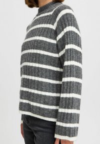 Pull à rayures grises et blanches, texture côtelée, col rond, manches à revers, coupe légèrement ample. Le matériau semble doux et chaud.