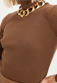 Top de cuello alto de canalé marrón con mangas largas, acompañado de un collar de cadena dorada gruesa que presenta eslabones texturizados.