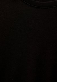 Schwarzer Baumwollstoff mit glatter Textur; hat einen fein gerippten Ausschnitt und minimale Nähdetails.