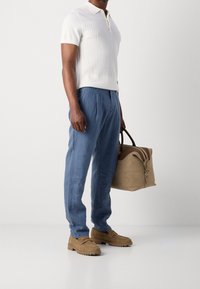 Gebreide witte polo, lichtblauwe linnen broek, tan suède schoenen en een bruine leren handtas met contrasterende accenten.