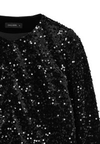 Top nero con paillettes, dal collo rotondo e senza chiusura visibile. Paillettes circolari dense creano una superficie strutturata e lucente.
