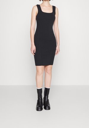 Schwarzes geripptes Kleid mit quadratischem Ausschnitt und figurbetontem Schnitt, kombiniert mit schwarzen Stiefeletten mit weißen Akzenten. Einfaches und elegantes Design.