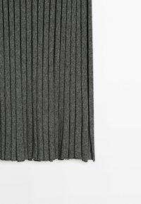 Jupe plissée en tissu gris foncé avec une texture côtelée verticale, suspendue droite sur un fond blanc.