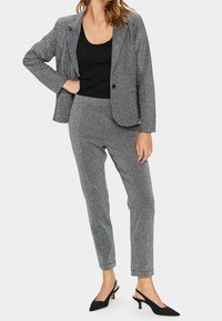 Szary, błyszczący garnitur z dopasowaną marynarką i zwężanymi spodniami. Tkanina ma lśniącą strukturę. W zestawie z czarnymi butami na obcasie typu slingback.