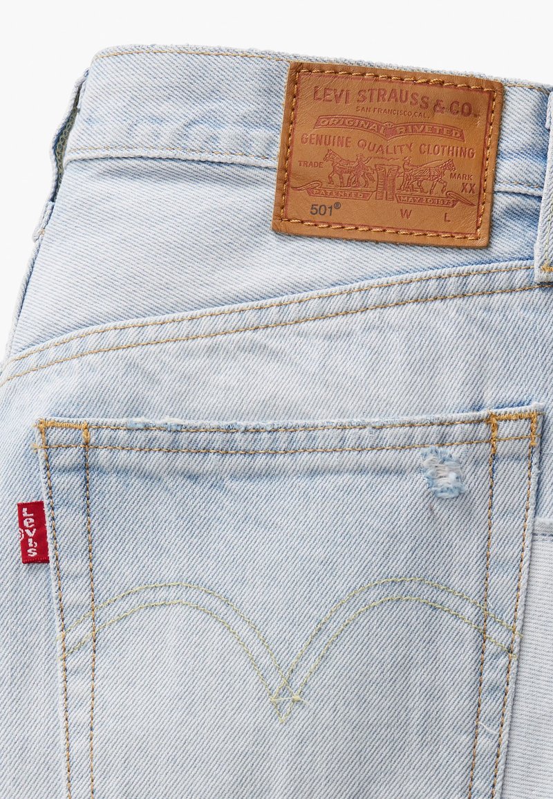 Jeans di denim azzurro chiaro con una toppa in pelle etichettata "Levi Strauss & Co." e un particolare motivo di cucitura gialla sulle tasche posteriori.