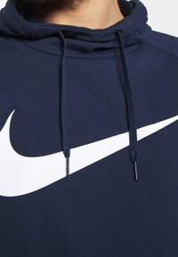 Primo piano di un hoodie blu navy con il logo Nike bianco a forma di baffo sul petto e cordini blu navy che pendono dal cappuccio.