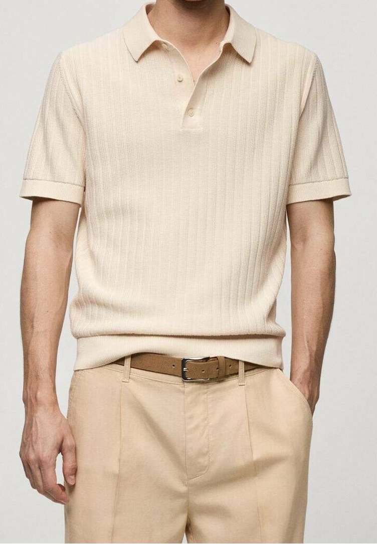 Homme portant un polo à manches courtes en maille beige rentré dans un pantalon beige avec une ceinture marron, debout avec une main dans la poche.
