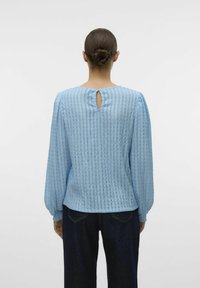 Heledsinine, tekstuuriga pluus, millel on vertikaalsed triibud, puffvarrukad ja võtmeaugu detail seljal. Valmistatud pehmest ja kergest kangast.