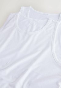 Két fehér pamut trikó együttes bemutatása, merész nyakkivágásokkal, sima textúrával és könnyű anyagból, enyhe redőzéssel.