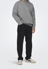 Sudadera con capucha gris y un bolsillo frontal, combinada con jeans de mezclilla negros. El calzado consiste en zapatillas deportivas de tono claro con un diseño de acento oscuro.