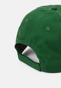 Boné de basebol verde com aba curva, feito de algodão. Apresenta detalhes de costura e orifícios de ventilação nas painéis superiores.