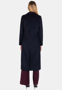 Cappotto di lana blu navy con maniche lunghe, colletto e taglio a media lunghezza; presenta una cucitura verticale sul retro e una texture semplice.