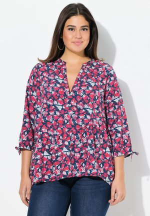 Top con stampa floreale che presenta foglie rosse, rosa e bianche su uno sfondo blu navy, con scollo a V e maniche a tre quarti. Design leggero e fluido.