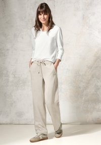 Leichtes weißes Langarmoberteil, kombiniert mit beigen Hosen mit Kordelzug. Strukturiertes Material und sportliche grün-graue Sneaker. Einfache Designelemente.