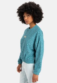 Türkiser Pullover mit strukturiertem Blattform-Muster, geripptem Ausschnitt und elastischen Bündchen. Verfügt über ein kleines Logo auf der Brust und einen lässigen Schnitt.