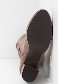 Botín de ante marrón con tacón bajo, cremallera lateral y suela de goma texturizada. Talla 37 visible impresa en la suela.