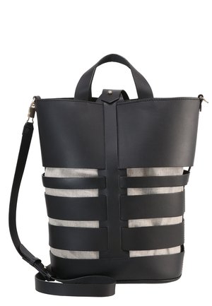 Czarna skórzana torba typu bucket z szerokimi poziomymi paskami na tle beżowej tkaniny, górnym uchwytem i odpinanym paskiem na ramię.