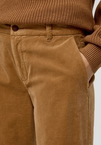 Bruine ribfluwelen broek met een textuurafwerking, zijzakken en een aansluitende taille. Voorzien van een knoopsluiting voor een veilige pasvorm.