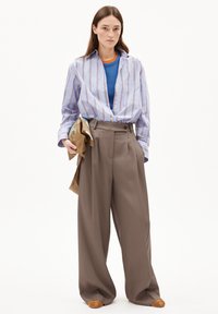 Blau-weiß gestreifte Hemdbluse, übereinander getragen mit einem blauen Oberteil, kombiniert mit hochgeschnittenen beigen Hosen und beigen Slippern.