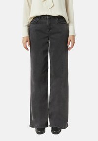 Czarne dżinsy o szerokich nogawkach z wysokim stanem, czterema kieszeniami i lekko wyblakłym wykończeniem. Połączone z jasnobarwną bluzką z długim rękawem.