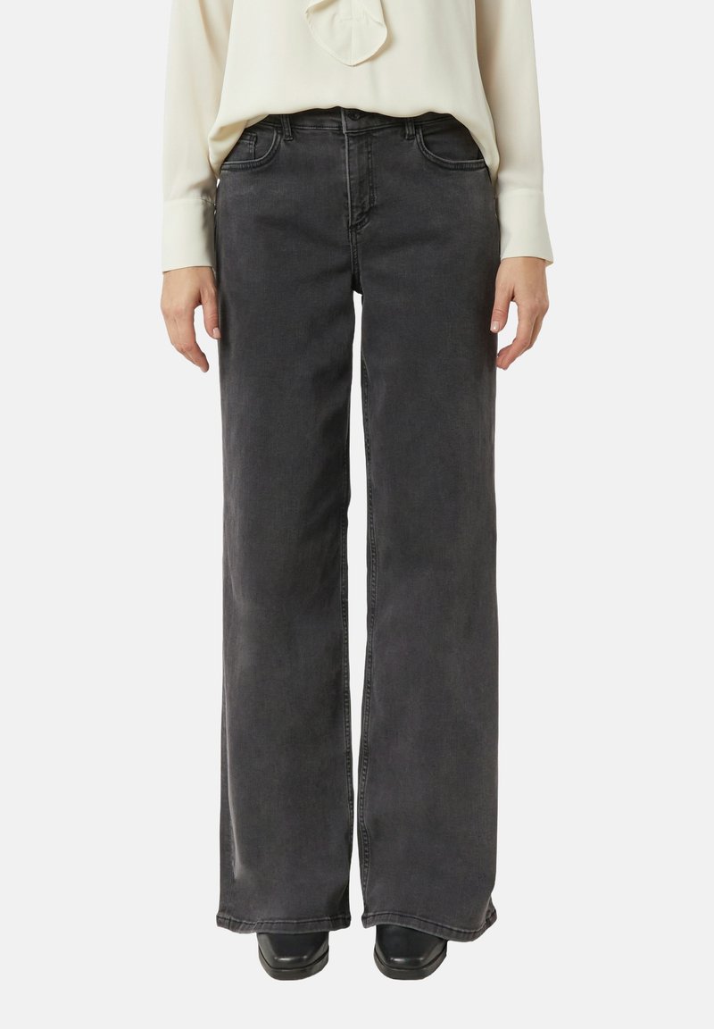 Czarne dżinsy o szerokich nogawkach z wysokim stanem, czterema kieszeniami i lekko wyblakłym wykończeniem. Połączone z jasnobarwną bluzką z długim rękawem.