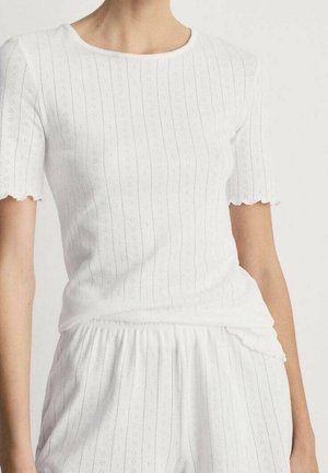 Haut blanc à manches courtes en maille côtes fines avec des motifs verticaux subtils et des bords de manches festonnés, porté avec un pantalon texturé assorti.