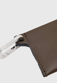 Brun læder kortholder med glat tekstur, sølv metal hardware, der har en krokklap og syning ved kanten.