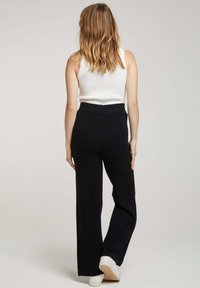 Pantalons larges noirs en tissu doux, avec une taille haute et un design épuré. Portés avec un débardeur blanc ajusté et des baskets blanches.