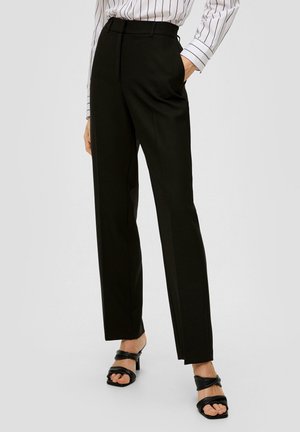 Schwarze taillierte Hose mit hoher Taille, mit scharfen Falten und seitlichen Taschen. Getragen mit schwarzen Absatzsandalen. Glatte Stofftextur.
