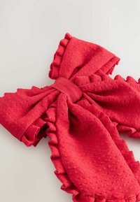 Un grand nœud en tissu rouge vif aux bords froncés est présenté sur un fond clair, mettant en valeur sa texture et son design élaboré.