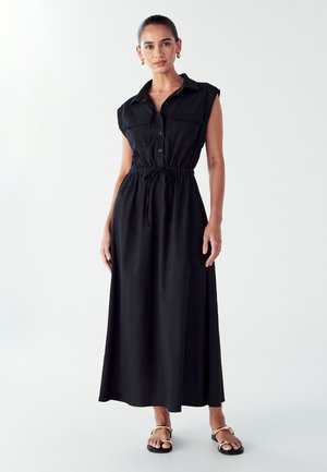 Black maxi dress with a button-down front, short sleeves, adjustable drawstring waist, and smooth fabric. Worn with flat sandals.