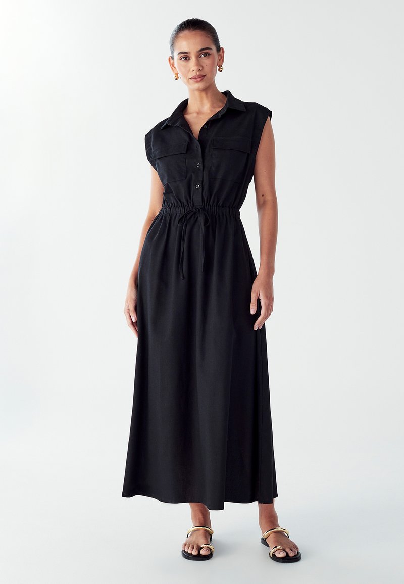 Schwarzes Maxikleid mit durchgehender Knopfleiste, kurzen Ärmeln, verstellbarem Kordelzug in der Taille und glattem Stoff. Getragen mit flachen Sandalen.