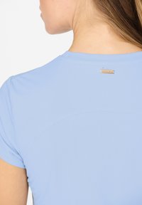 Hellblaues Sportshirt mit kurzen Ärmeln, glatter Textur, Rundhalsausschnitt und einem kleinen metallischen Markenetikett auf der Rückseite.