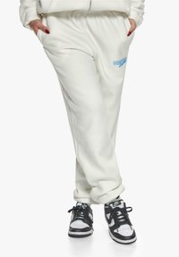 Hvite, myke, fleece joggebukser med elastisk midje og blå "DRIP" bokstaver. Kombinert med svart og hvite sneakers.