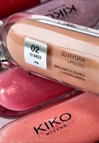 KIKO Milano 3D Hydra Lipgloss nella tonalità 02, con un tubetto trasparente, colore nude e finitura glitterata, presenta un'etichetta con i dettagli del prodotto.