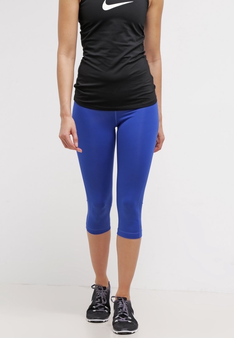 Czarny damski top bez rękawów z białym logo, zestawiony z dopasowanymi niebieskimi legginsami do kolan. Buty czarne z fioletowymi sznurowadłami.