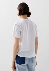 Hvid bomulds t-shirt med korte ærmer, rund halsudskæring, glat tekstur, vist fra ryggen, parret med lyseblå jeans med en mørk denimlap.