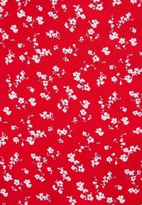 Punainen kangas, jossa on hajallaan valkoisia kukkakuvioita, pieniä kukkia ja herkkiä varret, luoden tekstuurisen ja elävän ilmeen.