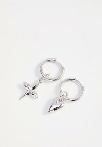 Srebrni obroči za ušesa z visečimi okraski, eden v obliki križa, drugi v obliki srca, na belem ozadju.