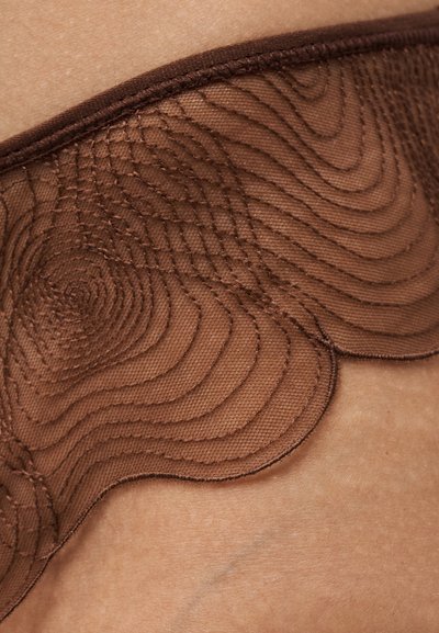 Gros plan de lingerie en tissu marron transparent avec des motifs de couture tourbillonnants sur la peau.