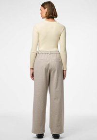 Lichtbeige geribbelde longsleeve top gecombineerd met hoogwaisted, wijde lichtbruine broek met achterzakken. Soepele stofstructuur.