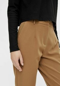 Beżowe spodnie o dopasowanym kroju, z bocznymi kieszeniami i gładką fakturą. Połączone z czarną prążkowaną bluzką z długim rękawem.