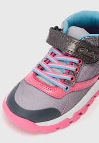 Zapato deportivo infantil con malla gris, acentos en rosa, cordones azules y rosas, y una correa de Velcro metálica oscura.
