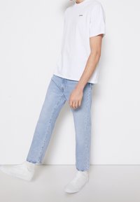 Weißes Baumwoll-T-Shirt mit kurzen Ärmeln, hellblaue gerade Jeans und weiße Sneakers. Einfaches, lässiges Design ohne sichtbare Muster.