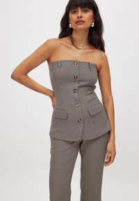 Hnedo-biely kockovaný top bez ramienok s priliehavým strihom, prednými gombíkmi a dvoma bočnými vreckami. Kombinovaný s zodpovedajúcimi upravenými nohavicami.