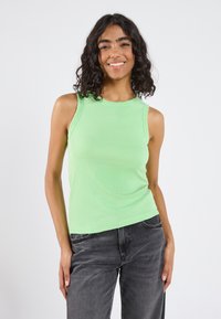 Grøn ribbet tanktop med en tætsiddende pasform og rund halsudskæring, parret med mørkegrå denimjeans. Standard stoftekstur.