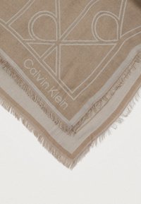 Beige villasekoitusscarf, jossa on kudottu geometrinen kuosi, fringet ja hienovaraisesti kohokuvioitu "Calvin Klein" -logo reunassa.