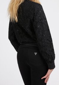 Black lace cropped sweatshirt with patterned texture and puffed sleeves, paired with high-waisted black jeans featuring a triangle logo on the pocket.
